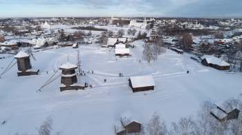 A snowy landscape featuring traditional wooden buildings and people walking in a historic village setting.