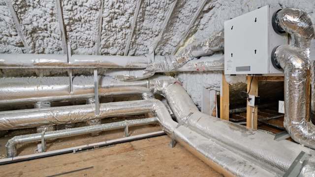 An attic with insulated ductwork and a ventilation system on the wall.