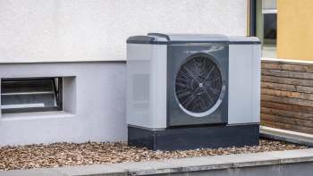 A modern heat pump unit placed beside a building's exterior wall with mulch landscaping.