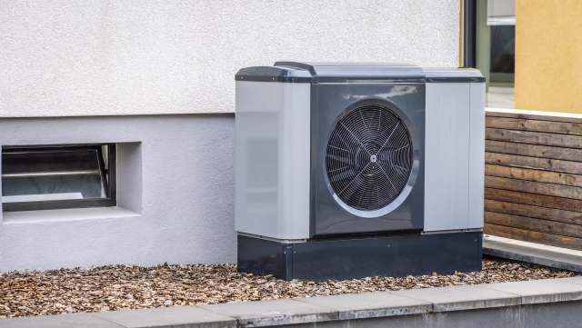 A modern heat pump unit placed beside a building's exterior wall with mulch landscaping.