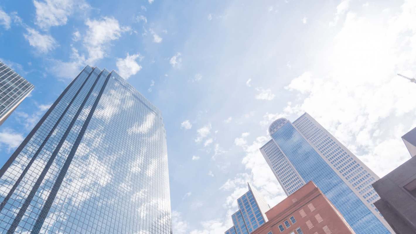 Tall skyscrapers rise against a bright sky with scattered clouds.