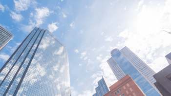 Tall skyscrapers rise against a bright sky with scattered clouds.