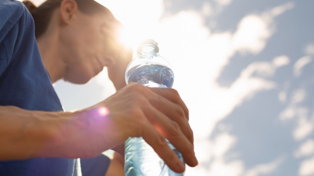 A person holding a water bottle with sunlight creating a halo effect behind them.