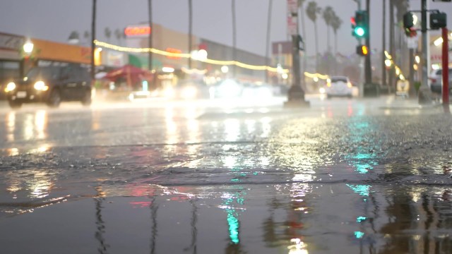 A city street is drenched in rain, with blurred car lights reflecting on the wet pavement.