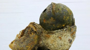 An ancient, rusted helmet embedded in a weathered rock formation.
