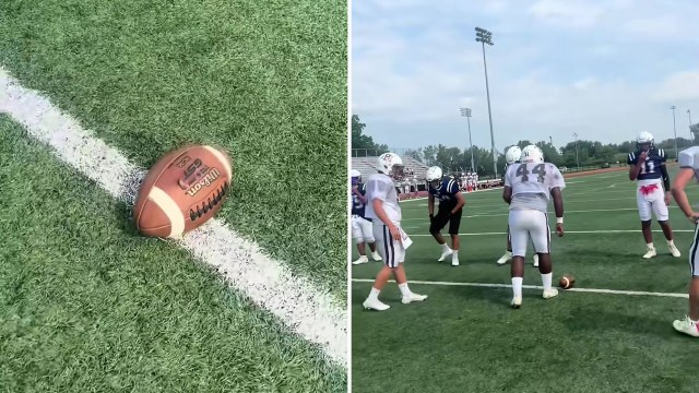 A football on the field next to players practicing during a team training session.