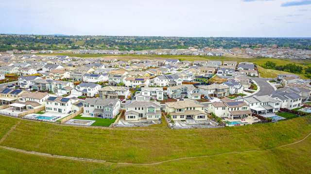 Aerial view of a suburban neighborhood with various houses and green areas on a hillside.