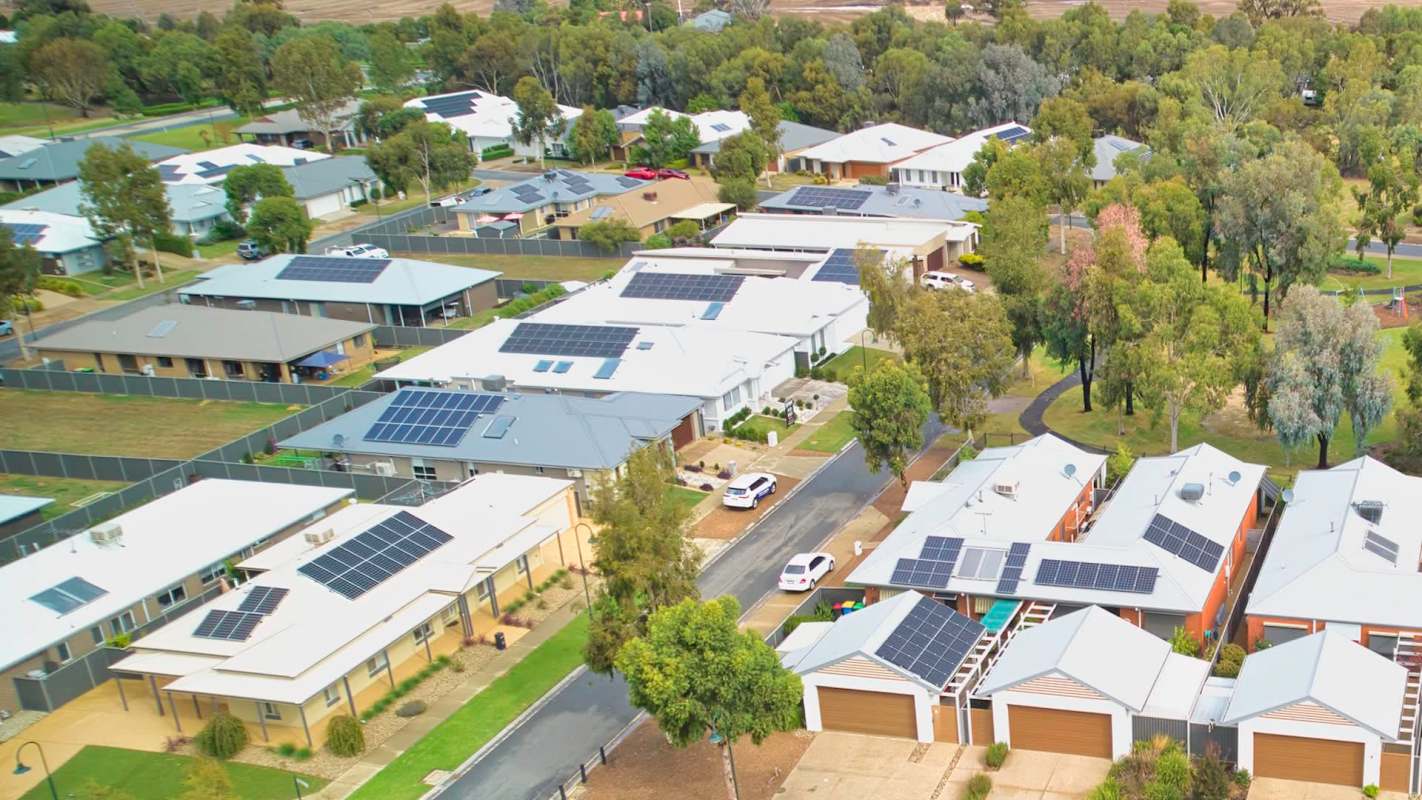 Aerial view of a suburban neighborhood featuring homes with solar panels and green trees.