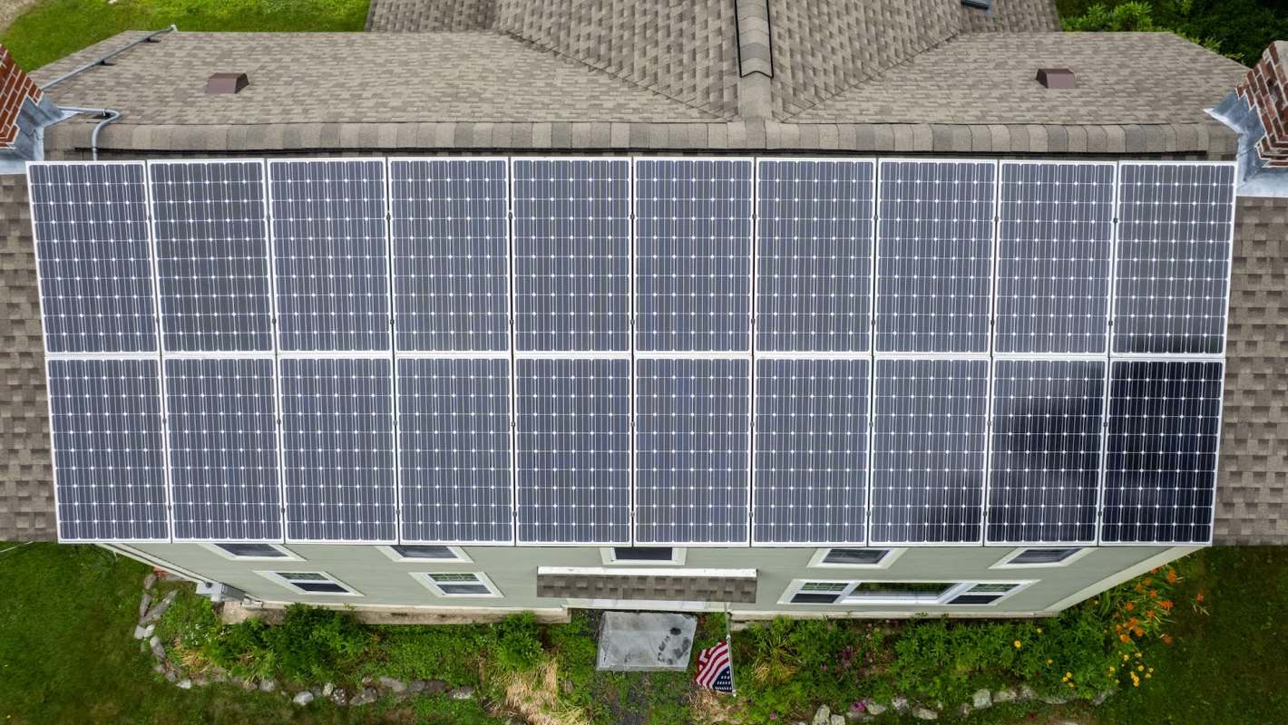 A rooftop covered with solar panels, alongside a green lawn and a small American flag.