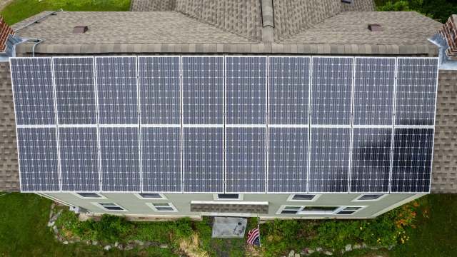 A rooftop covered with solar panels, alongside a green lawn and a small American flag.