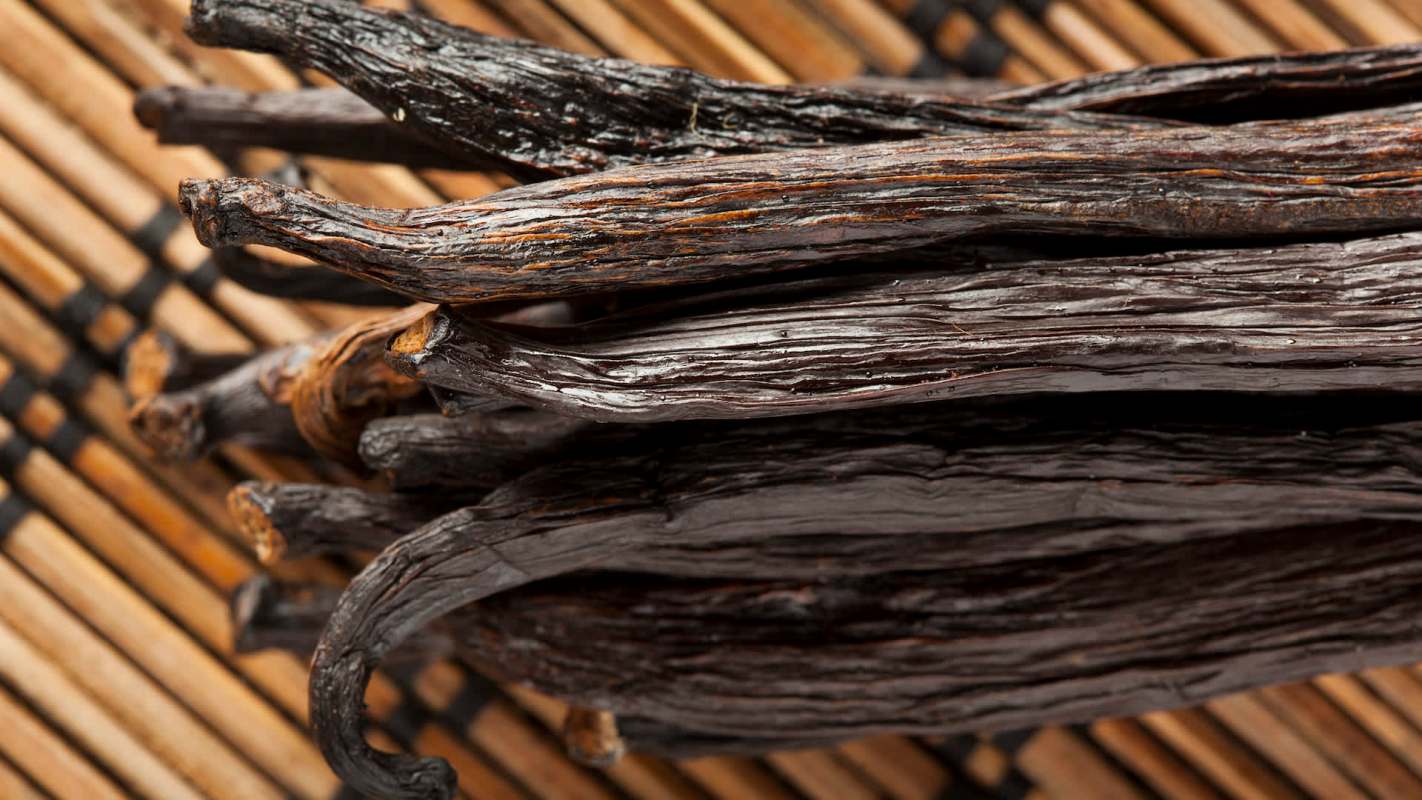 A close-up of dark, dried vanilla pods arranged over a bamboo mat.