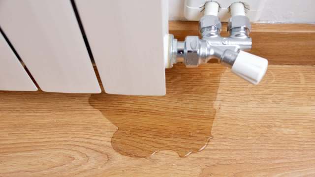 A radiator with a water leak pooling on a wooden floor.