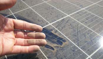 A hand with dirt on the fingers is positioned over a dusty solar panel surface.