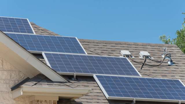A row of solar panels installed on a residential roof under a clear blue sky.