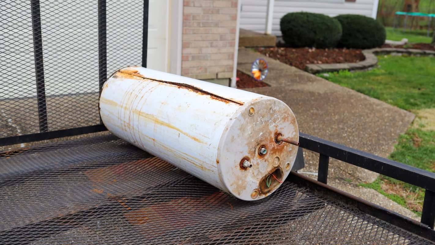 An old gas water heater sits on a trailer outside of a house.