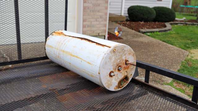 An old gas water heater sits on a trailer outside of a house.