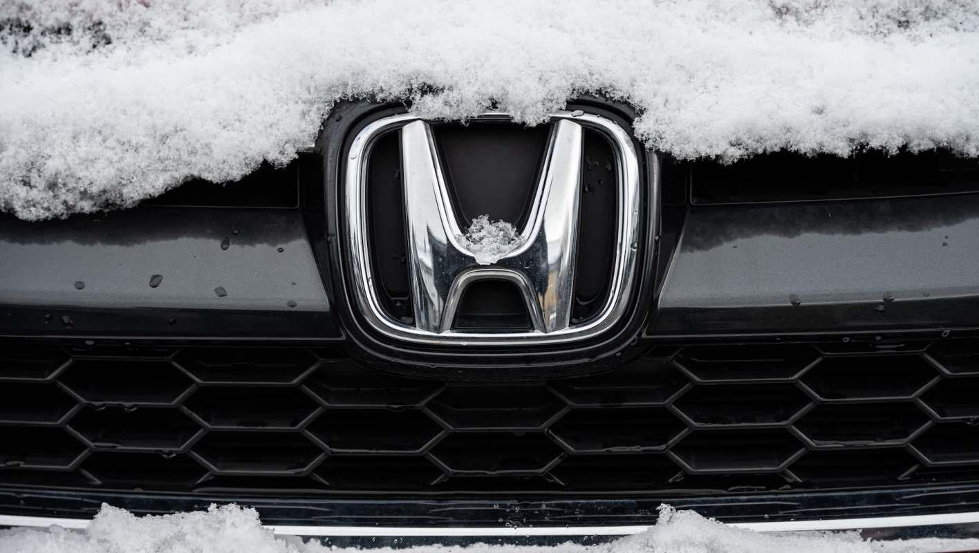 A close-up of a Honda logo partially covered in snow on a black car.