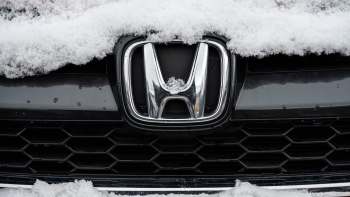 A close-up of a Honda logo partially covered in snow on a black car.