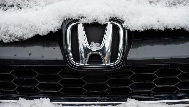 A close-up of a Honda logo partially covered in snow on a black car.