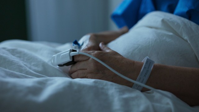 A person's hands resting on a bed with a medical device attached.