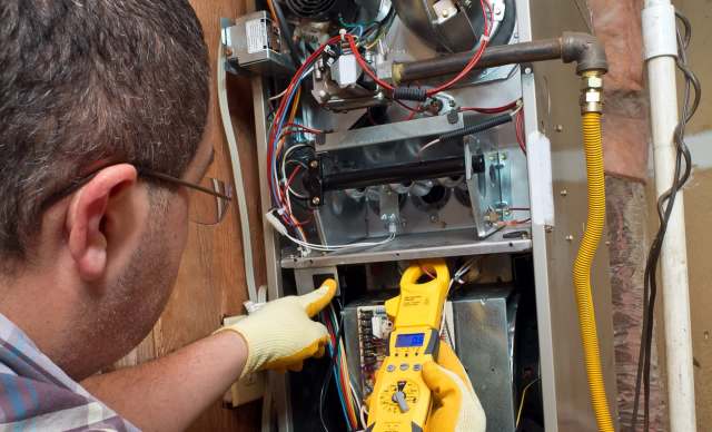 A technician uses a multimeter to inspect a furnace.