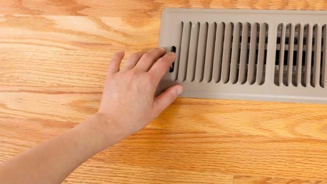A hand adjusting a vent on a floor.