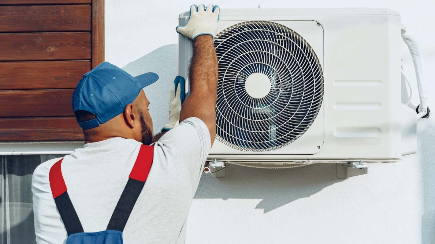 A technician in gloves installs an outdoor air conditioning unit on a wall.