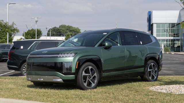 A green electric SUV parked on grass in front of a dealership with other vehicles nearby.