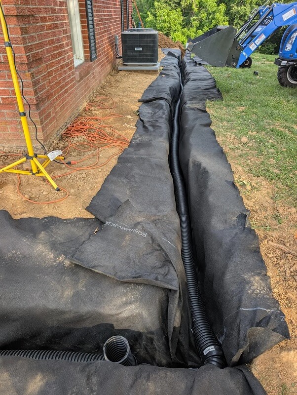 A trench being prepared for drainage with a pipe. 