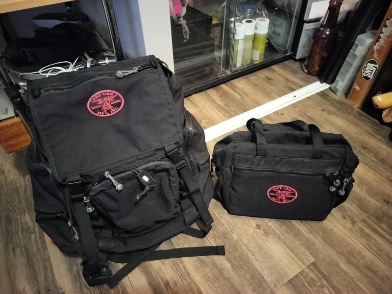 A large Red Oxx bag and a smaller one on a wooden floor.