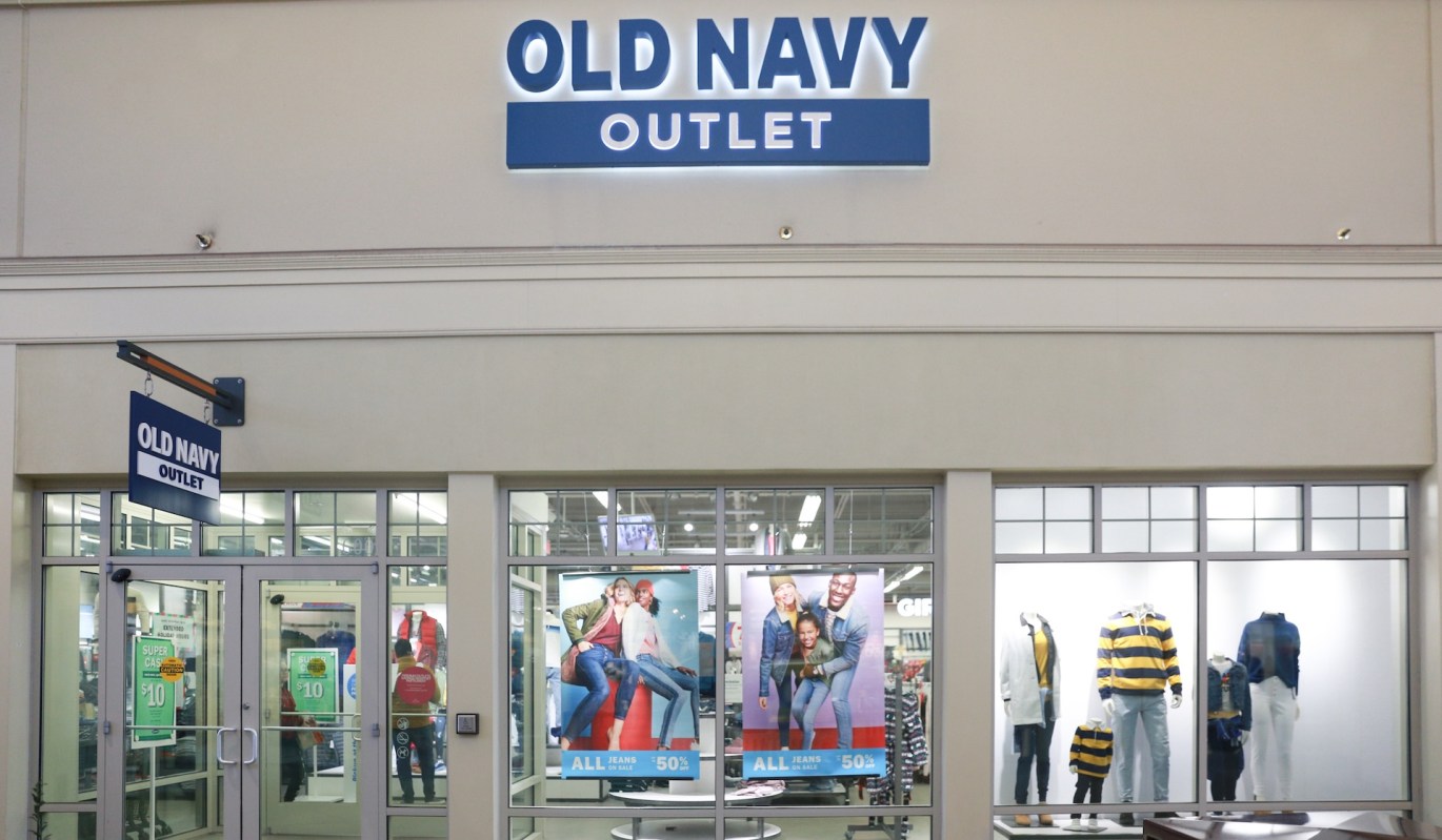 An Old Navy Outlet store front displaying promotional posters and mannequins dressed in casual clothing.