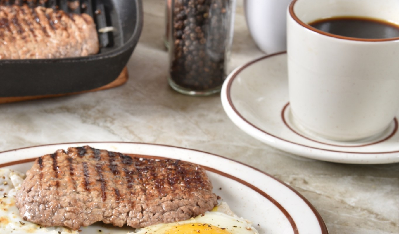 A grilled steak and fried egg on a plate with a cup of coffee.