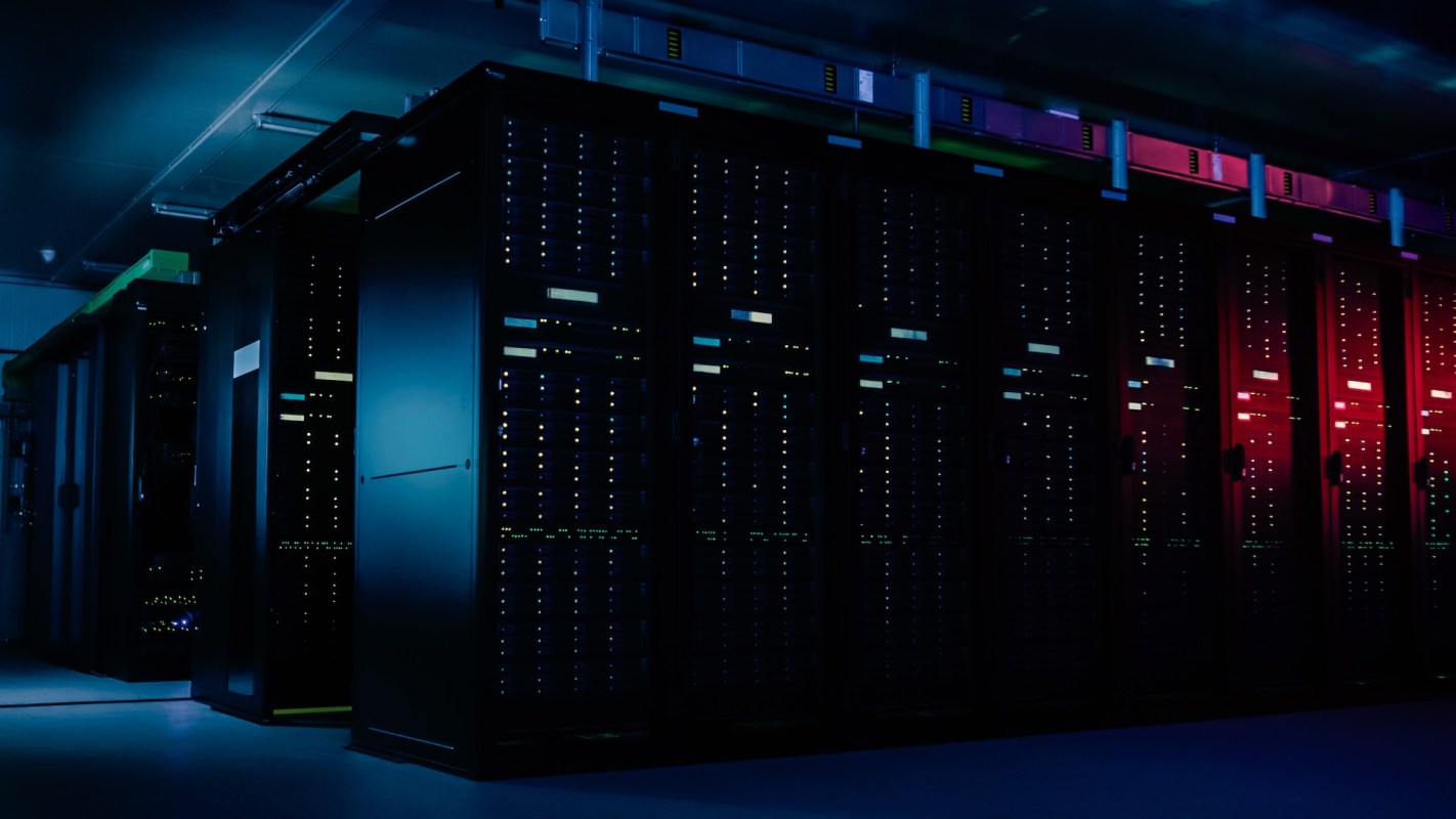 A dimly lit server room featuring tall racks filled with blinking lights and cables.