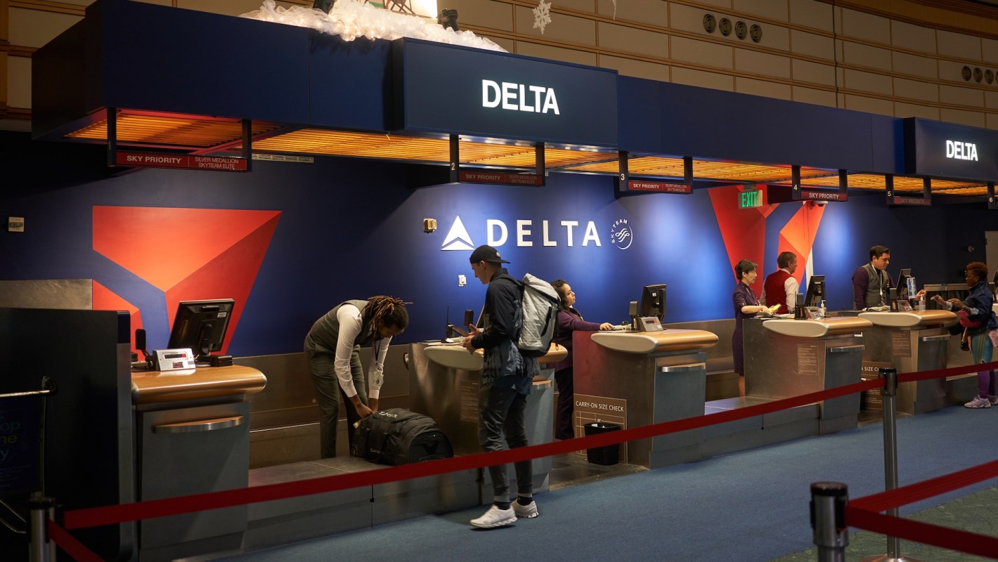 Staff assist passengers at Delta Airlines check-in counters at an airport.