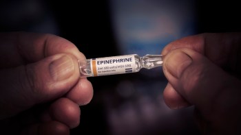 A close-up of hands holding a glass vial of epinephrine for injection.
