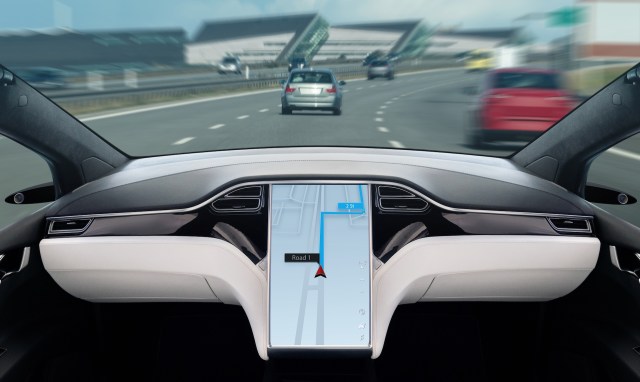 A view from the inside of a modern car with no steering wheel, displaying a navigation screen and blurred traffic ahead.
