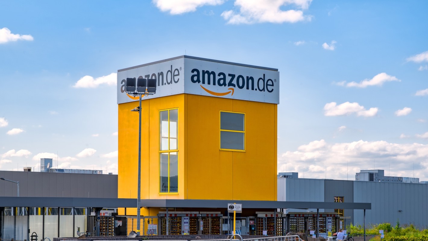 A bright yellow Amazon.de building with a large sign against a blue sky and scattered clouds.