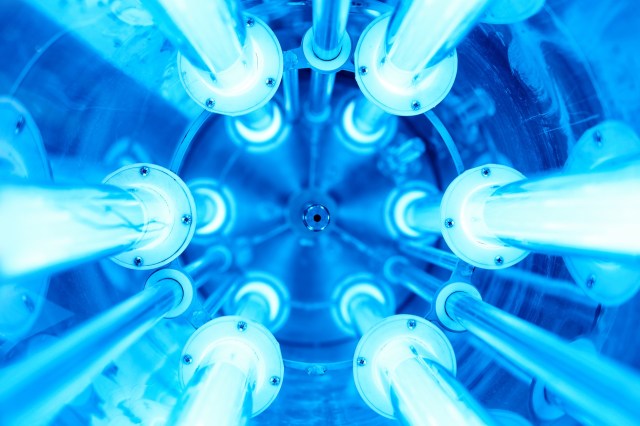 An upward perspective of metallic tubes illuminated by blue ultraviolet light within a circular, industrial setting.