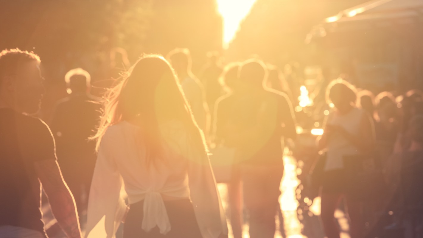 A crowd of people walking in a sunlit street during golden hour.