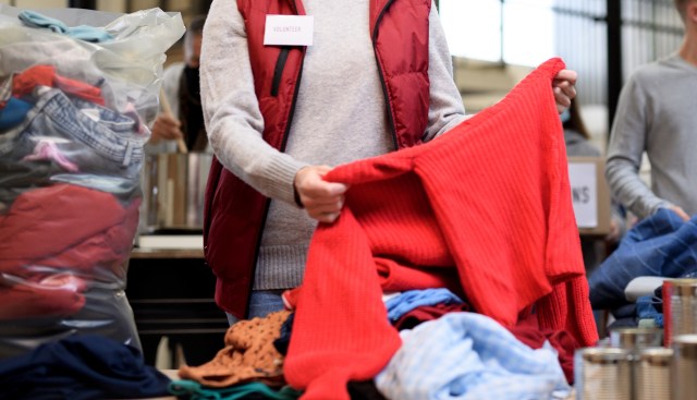 A volunteer sorts through a pile of clothing, holding a red sweater amid other assorted garments.