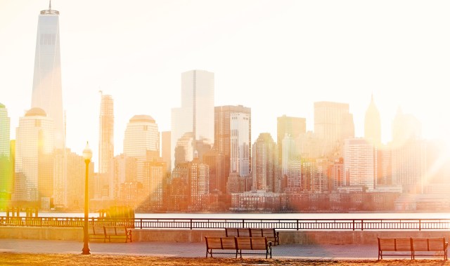 A sunlit view of a waterfront walkway overlooking a skyline with skyscrapers.