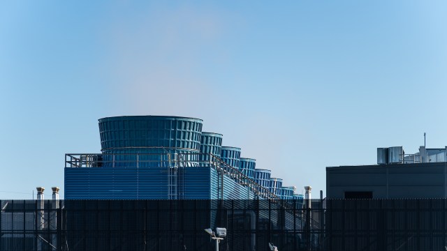 Cooling towers rise above the roof of a data center against a clear blue sky.