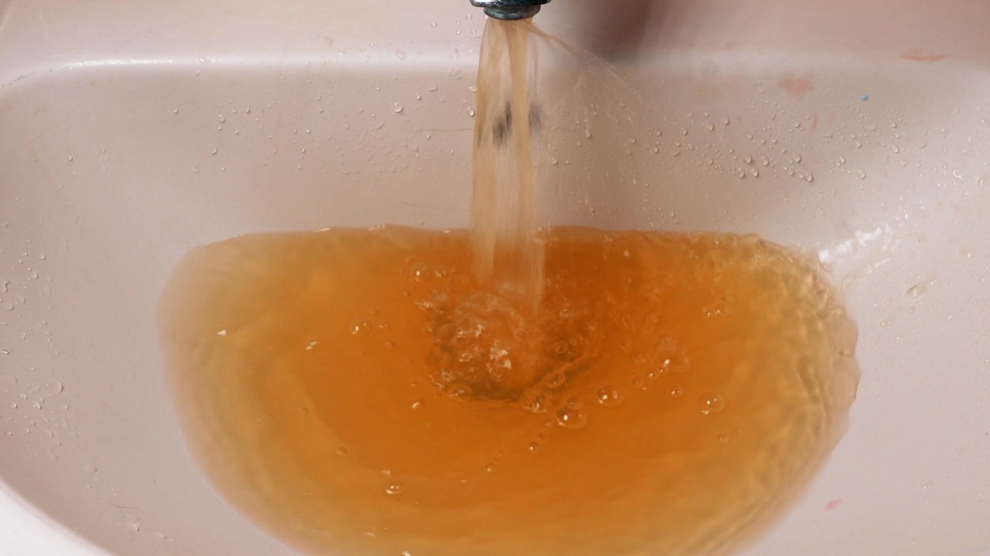 Brown water flows from a faucet into a sink, creating bubbles in the murky liquid.