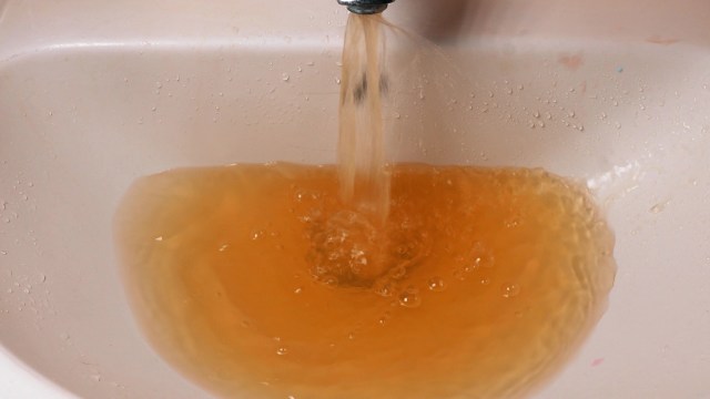 Brown water flows from a faucet into a sink, creating bubbles in the murky liquid.