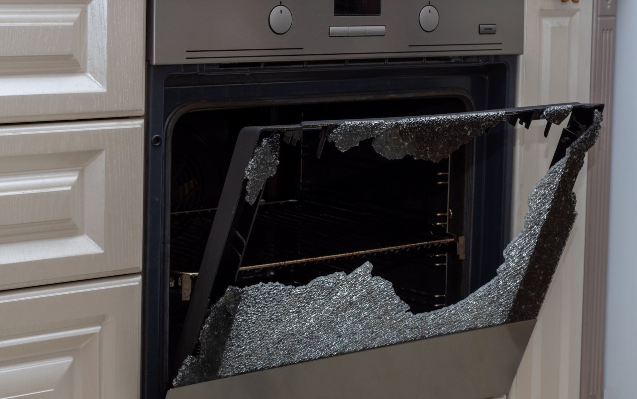 A broken oven door with shattered glass, revealing empty interior shelves.