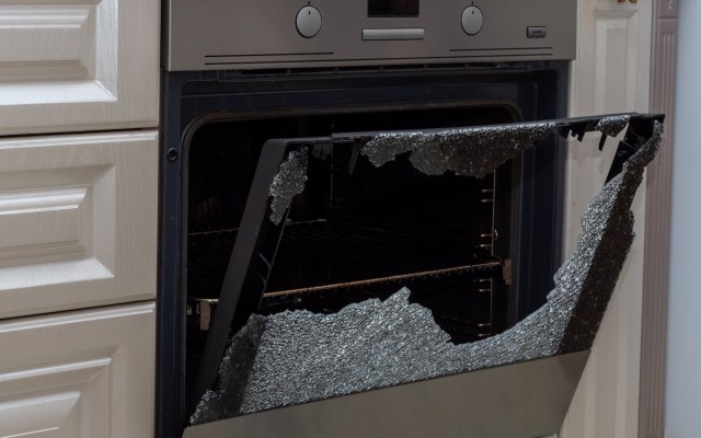 A broken oven door with shattered glass, revealing empty interior shelves.