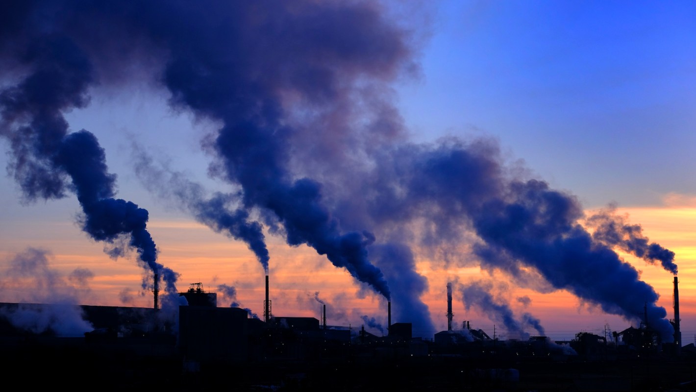 Industrial smokestacks release thick plumes of smoke at sunset.