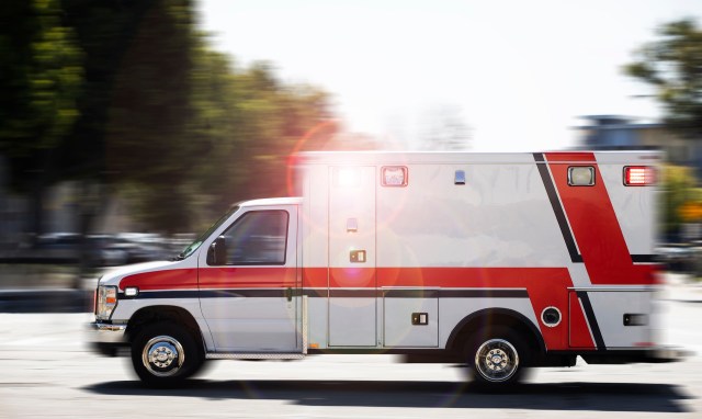 An ambulance races down a street, with lights flashing.