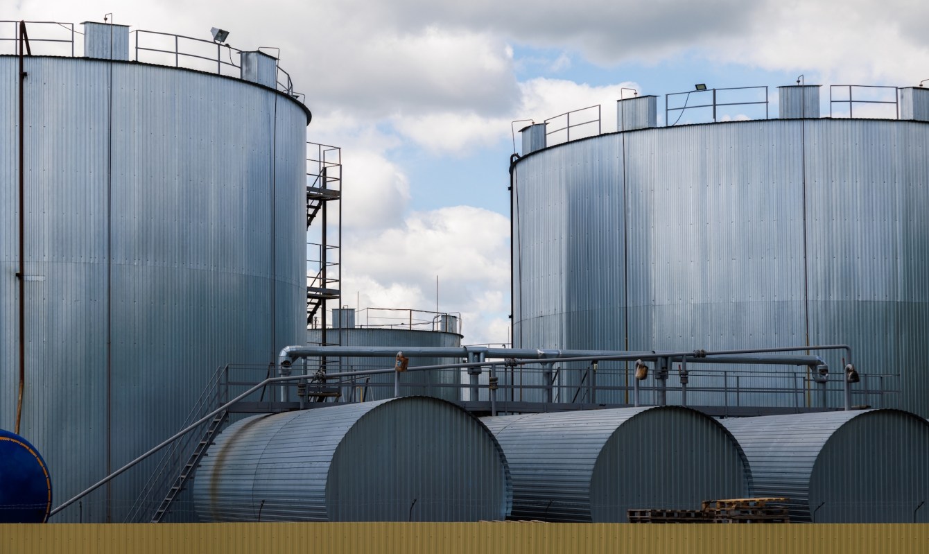 Large industrial storage tanks with metal siding under a cloudy sky.