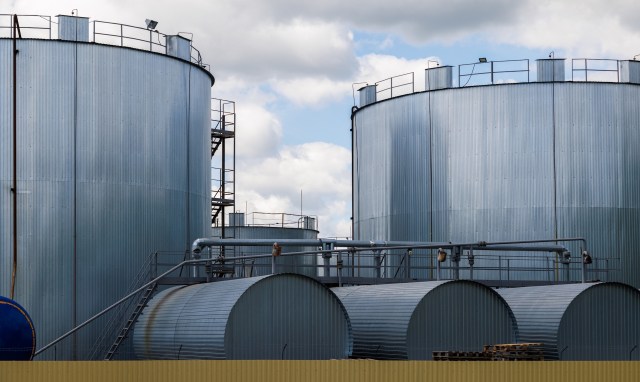 Large industrial storage tanks with metal siding under a cloudy sky.